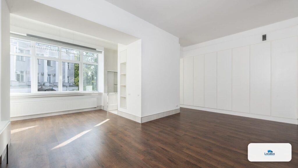 Chambre vide avec parquet et grande fenêtre après le démontage des meubles